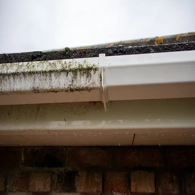 A side-by-side comparison showing a dirty section of guttering next to a sparkling clean white uPVC fascia and gutter after being washed by Crystal Clean Windows.