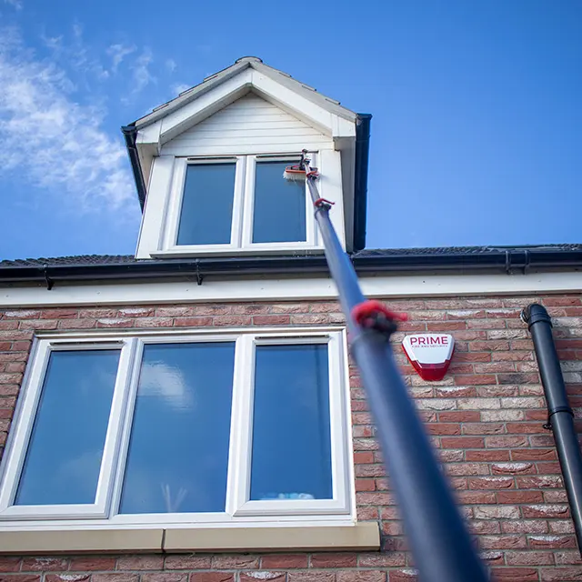 Professional window cleaning using a high-reach water-fed pole system to clean upper-story dormer windows on a brick house.